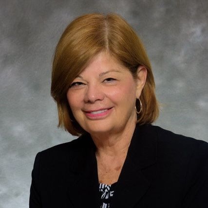 A woman wearing a black jacket and earrings smiles for the camera