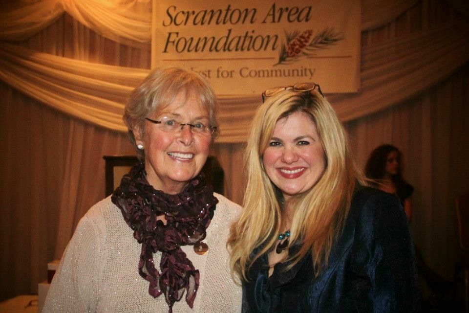 Two women are posing for a picture in front of a scranton area foundation sign