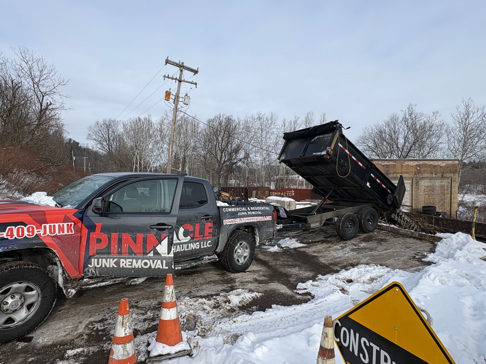 A junk removal truck with raised dump bed in a snowy construction zone in Latrobe, Pennsylvania.