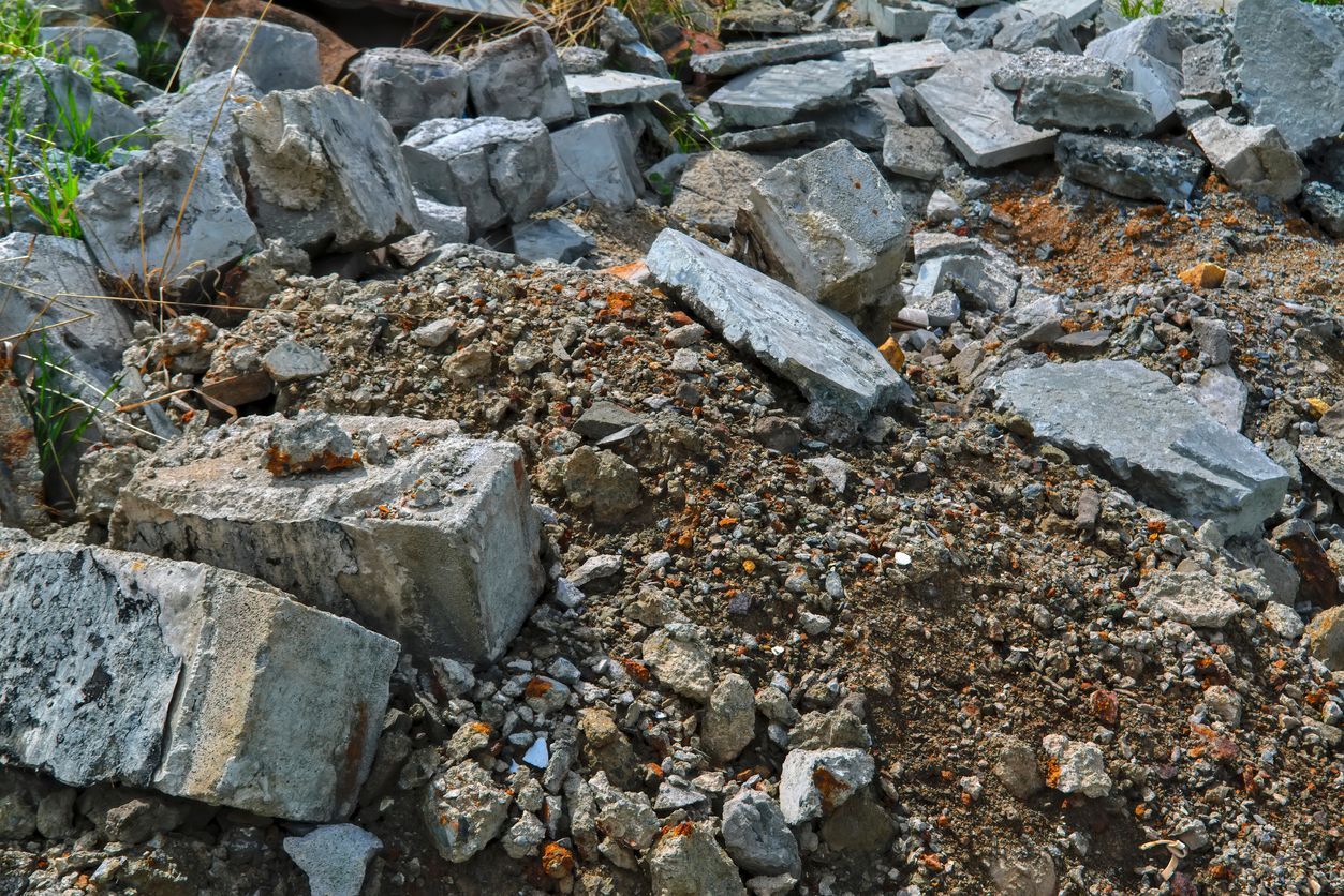 Pile of broken concrete debris with exposed earth and a few green shoots.