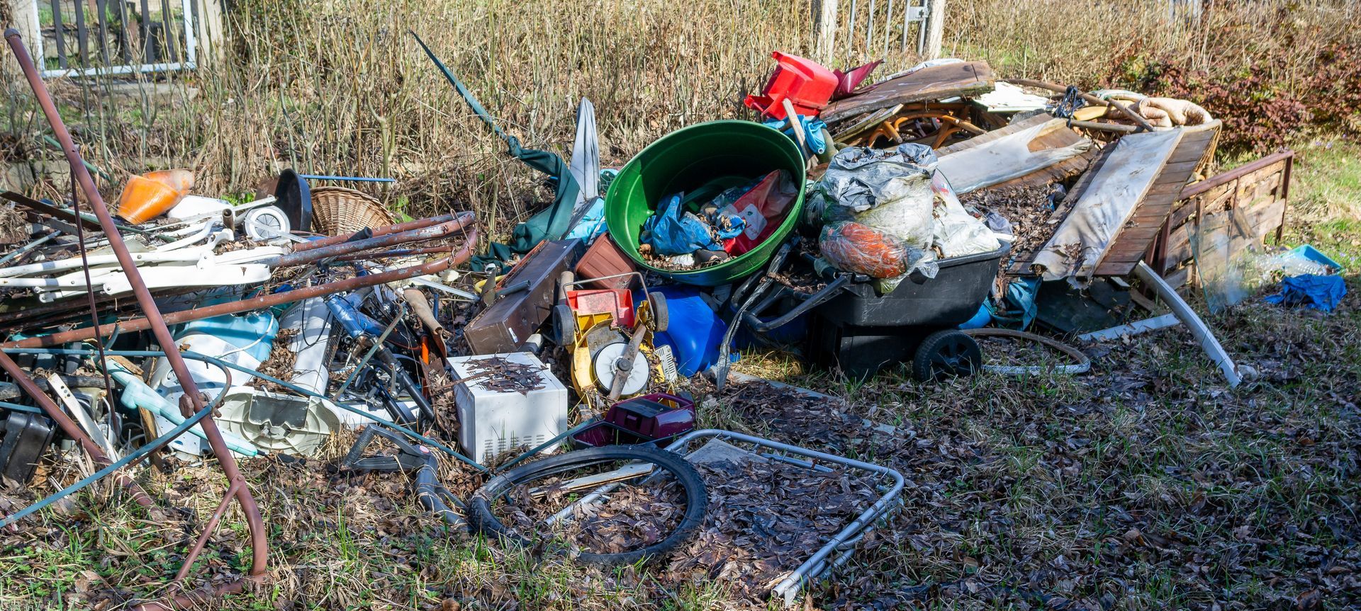 Pile of trash including a green bucket, scattered on brown grass.