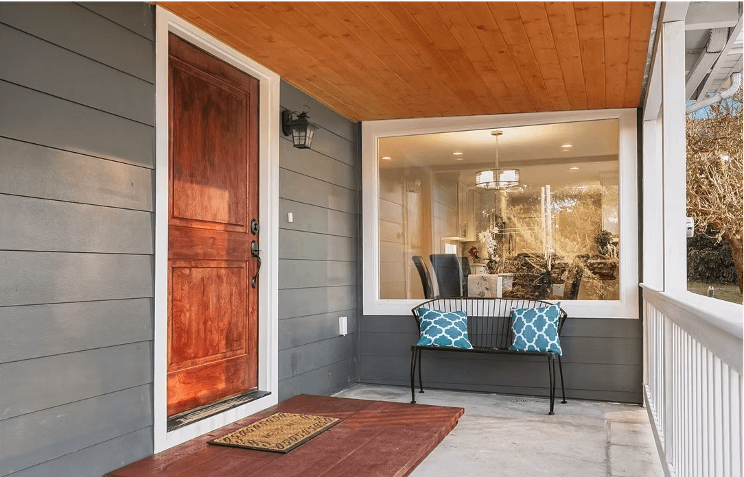 The front porch of a house with a bench and a large window.