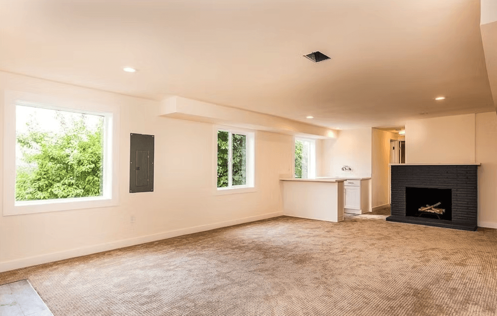 An empty living room with a fireplace and two windows.