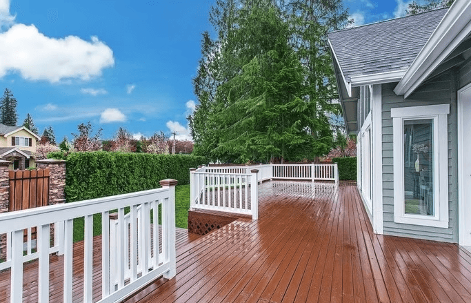 A large wooden deck with a white railing in front of a house.