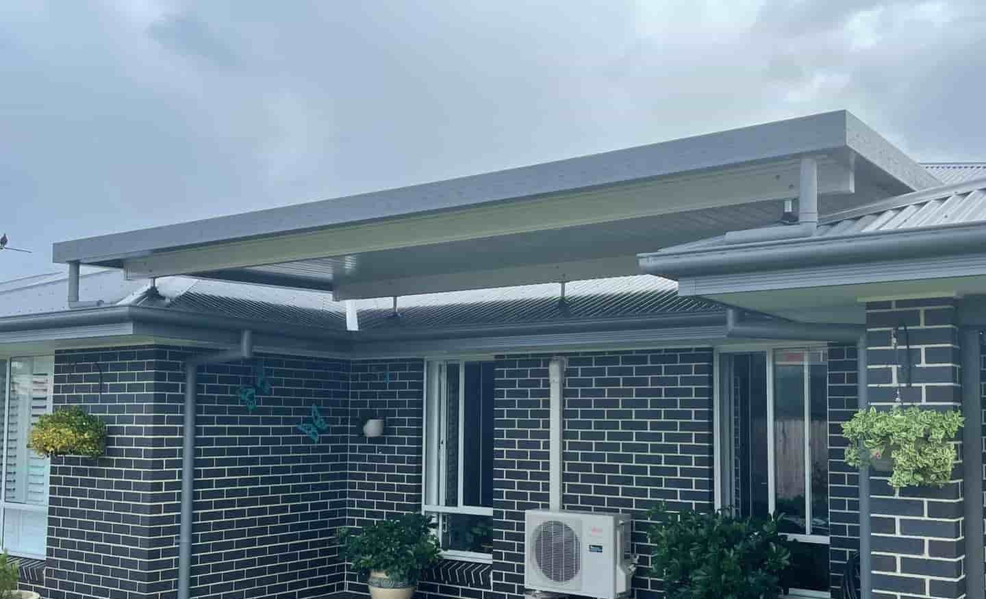 A Black Brick House With A White Air Conditioner On The Side Of It — Caprice Home Additions In Taree, NSW