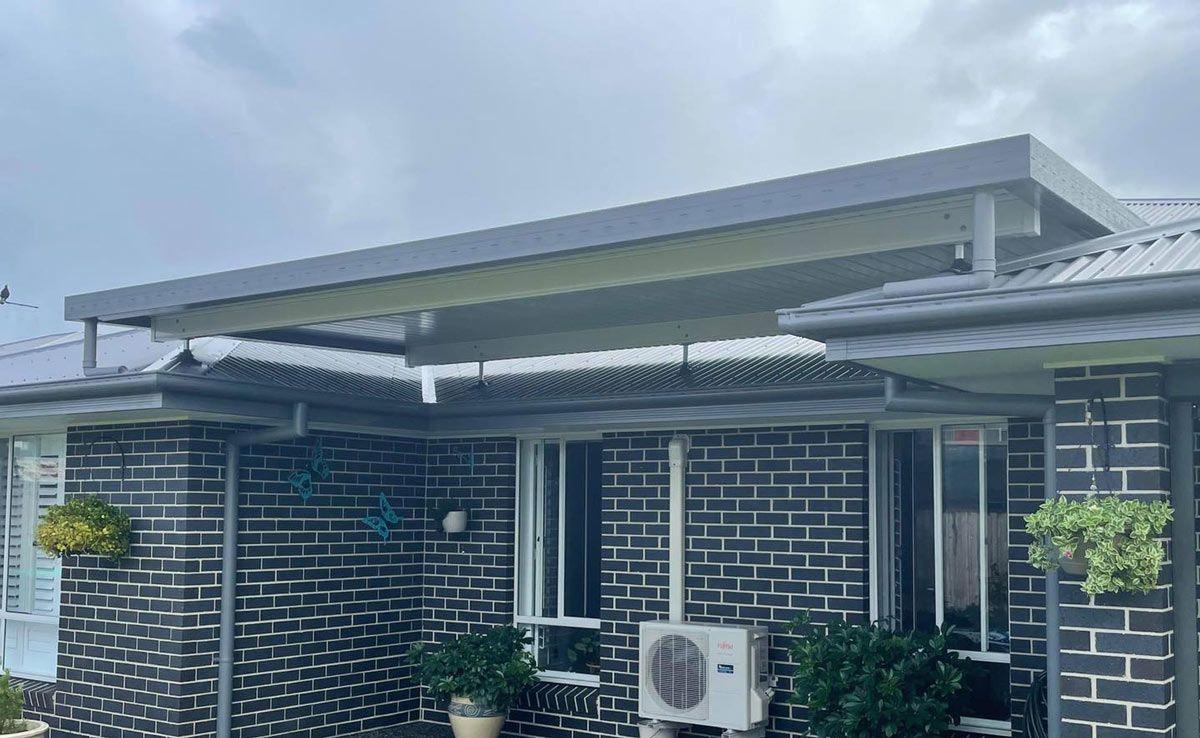 A Black Brick House With A White Air Conditioner On The Side Of It — Caprice Home Additions In Tuncurry, NSW