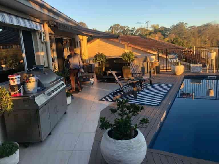 A Man Is Standing On A Patio Next To A Swimming Pool — Caprice Home Additions In Taree, NSW