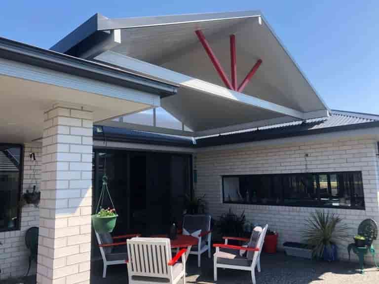 A White Brick House With A Patio Area With A Table And Chairs Under An Awning — Caprice Home Additions In Taree, NSW
