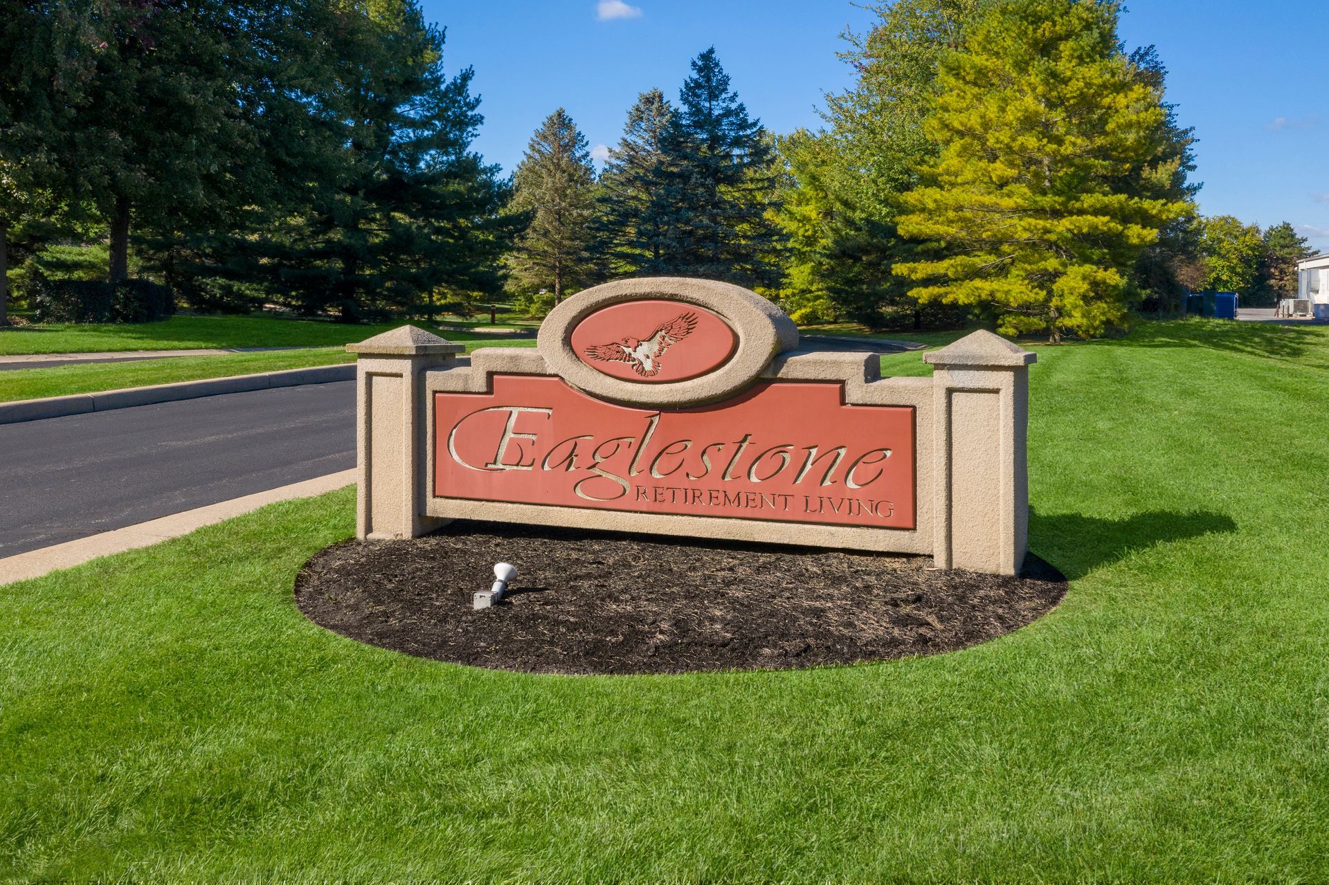 Eaglestone community sign in front of green grass and trees. The sign has an oval logo and red lettering.