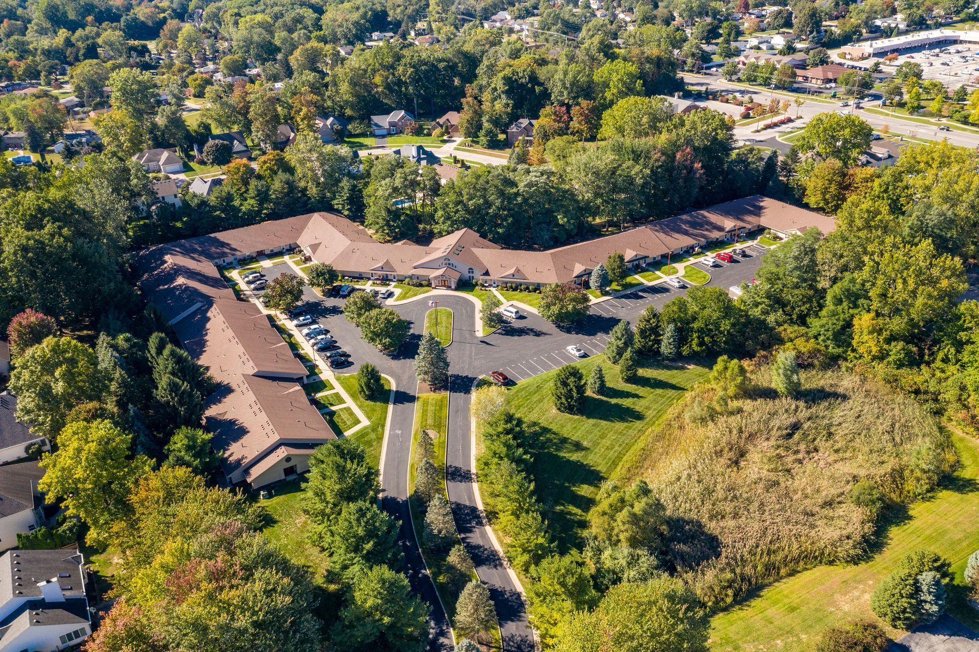Aerial view of a long, low, brown-roofed building surrounded by trees and green lawns, with parking.