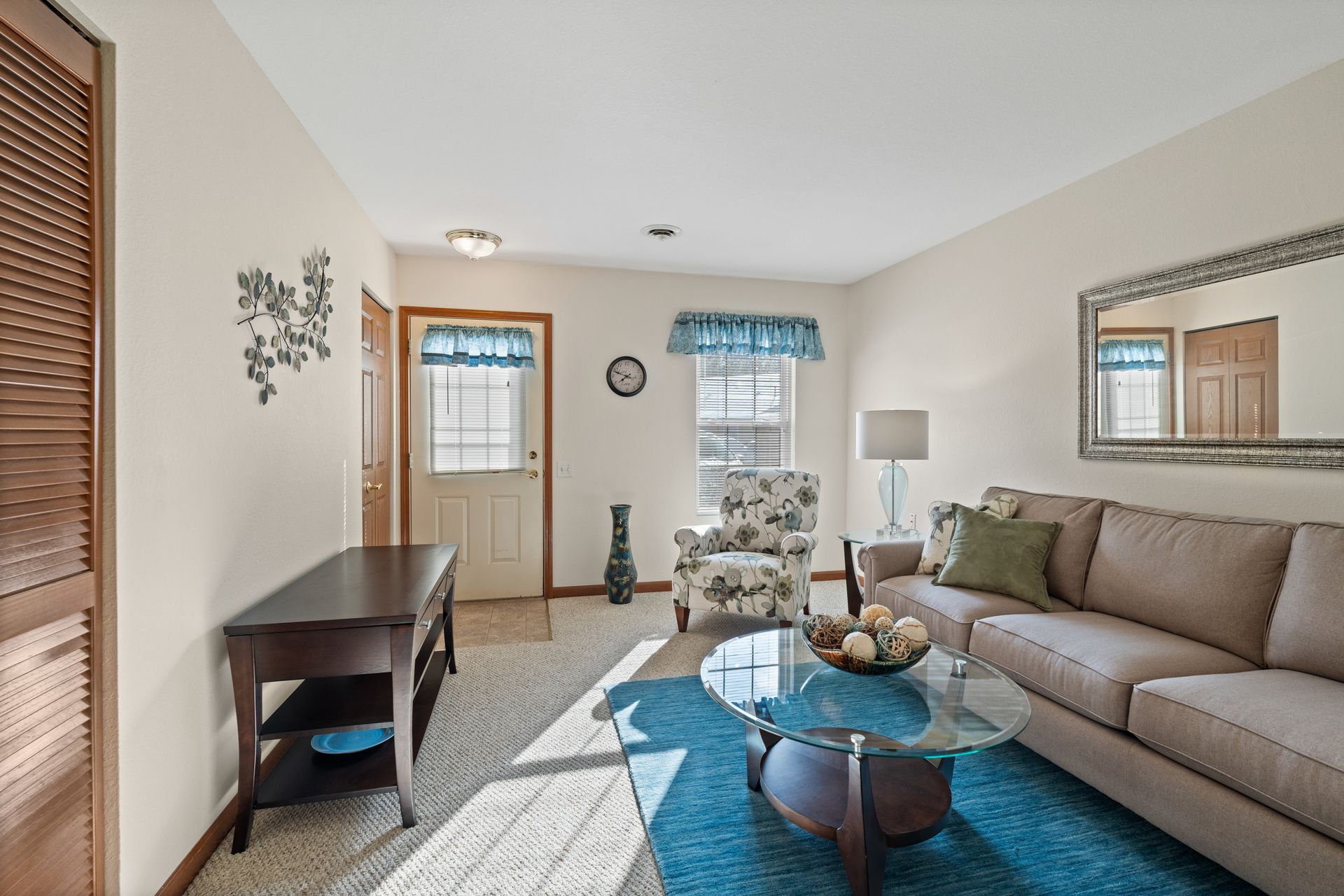 Photo of a living room with a tall window and a window on the door, both allowing for plenty of natural lighting