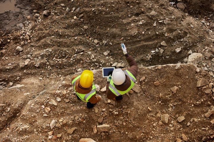 two industrial workers wearing reflective jackets standing on mining worksite outdoors using digital tablet, 