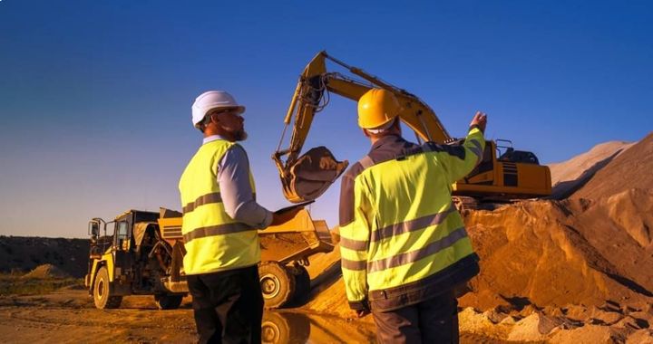 Two construction workers are standing in front of a bulldozer at a mining  site.
