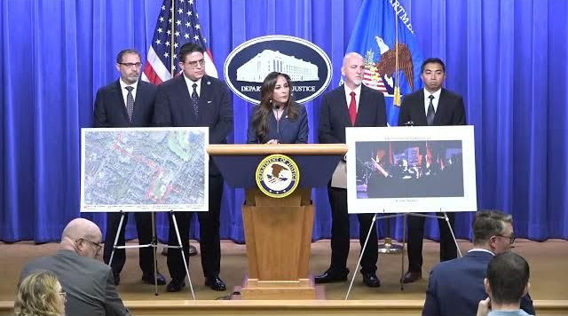 Conferencia de prensa con funcionarios detrás de un podio, diagramas e imágenes proyectadas. Fondo azul con banderas.