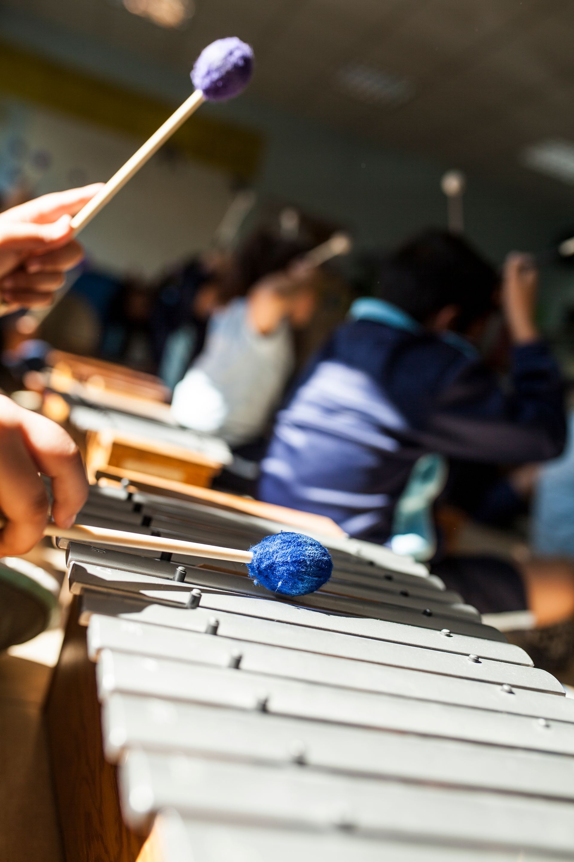 A person is playing a xylophone with a purple mallet.