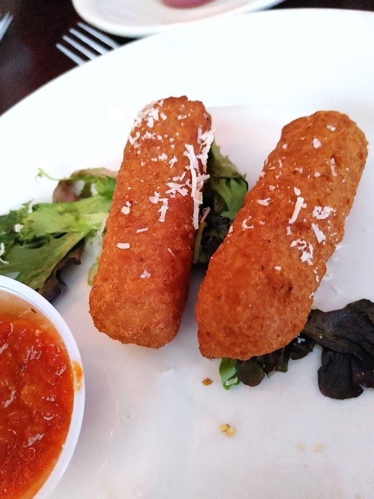 Two fried food sticks on a white plate with a side of salsa