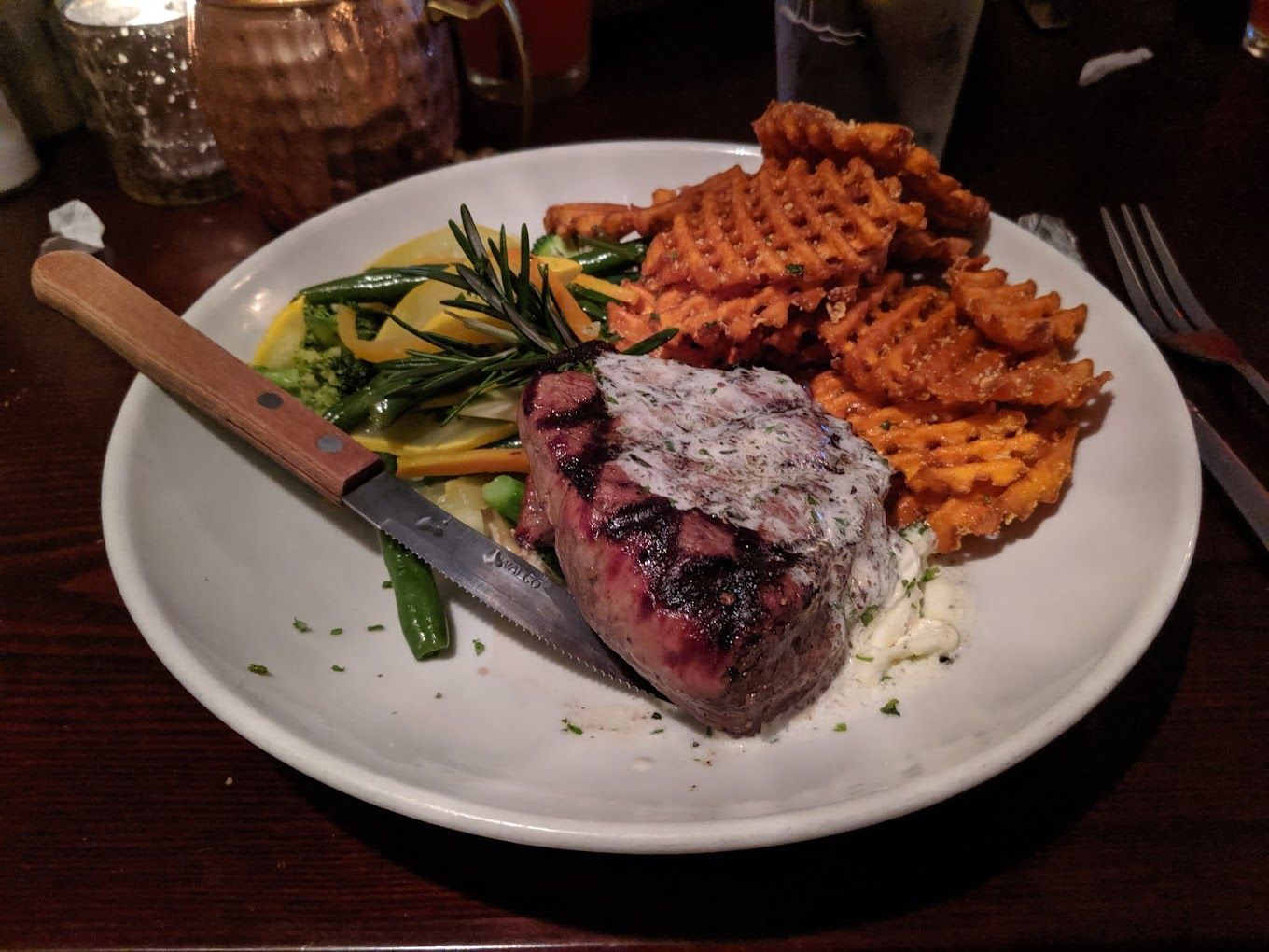 A plate of food with a steak vegetables and waffle fries