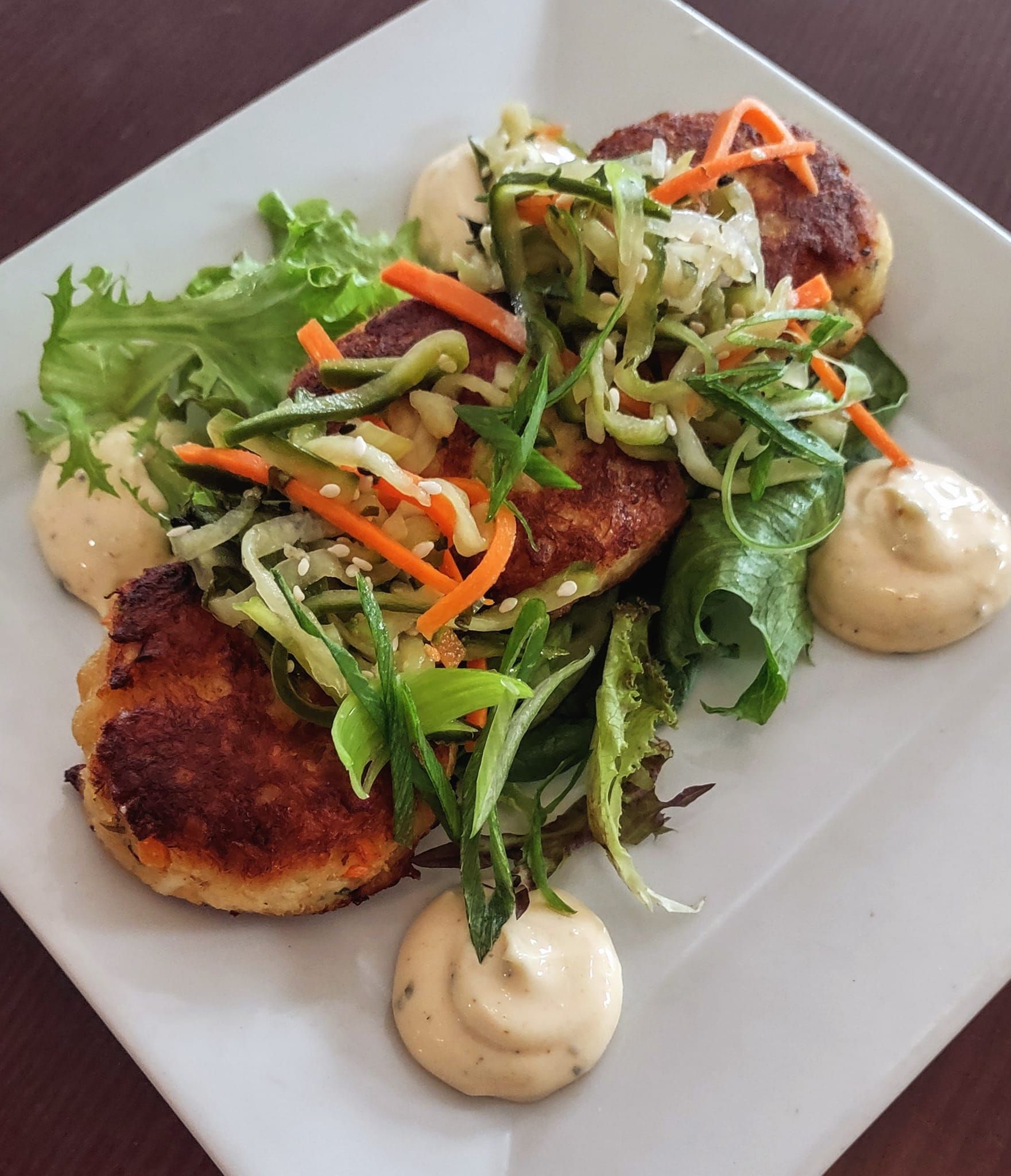 A white plate topped with crab cakes and vegetables