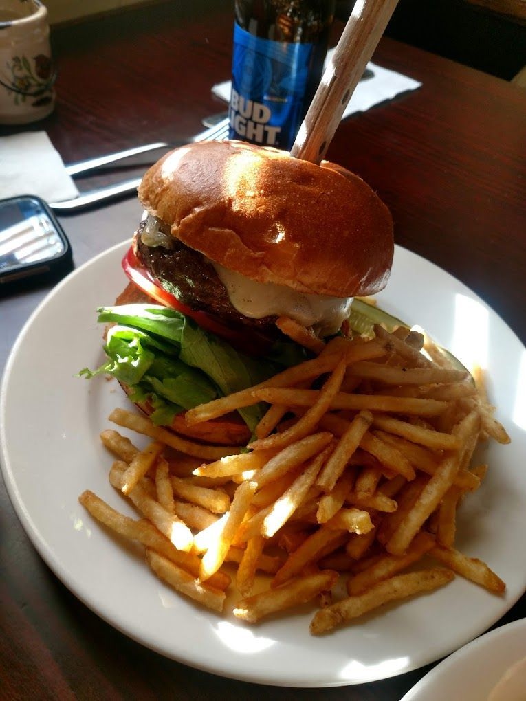 A hamburger and french fries on a white plate with a bud light bottle in the background