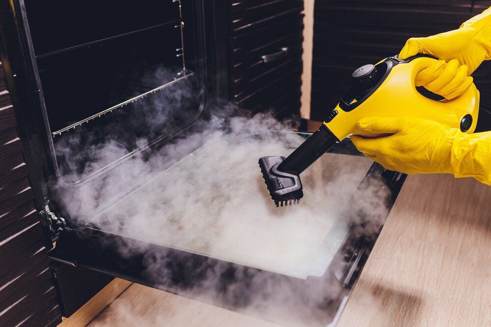 A staff member of Berkshire cleaning using steam cleaning to disinfect an oven