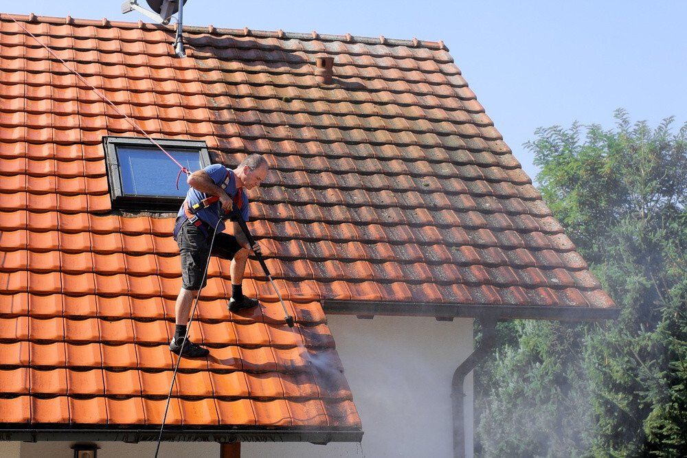 A hanged cleaner with a high pressure water gun standing on the roof of a house during pressure washing of the roof
