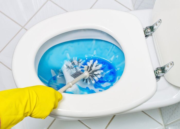A cleaner washing the toilet basin with deodorizing agent