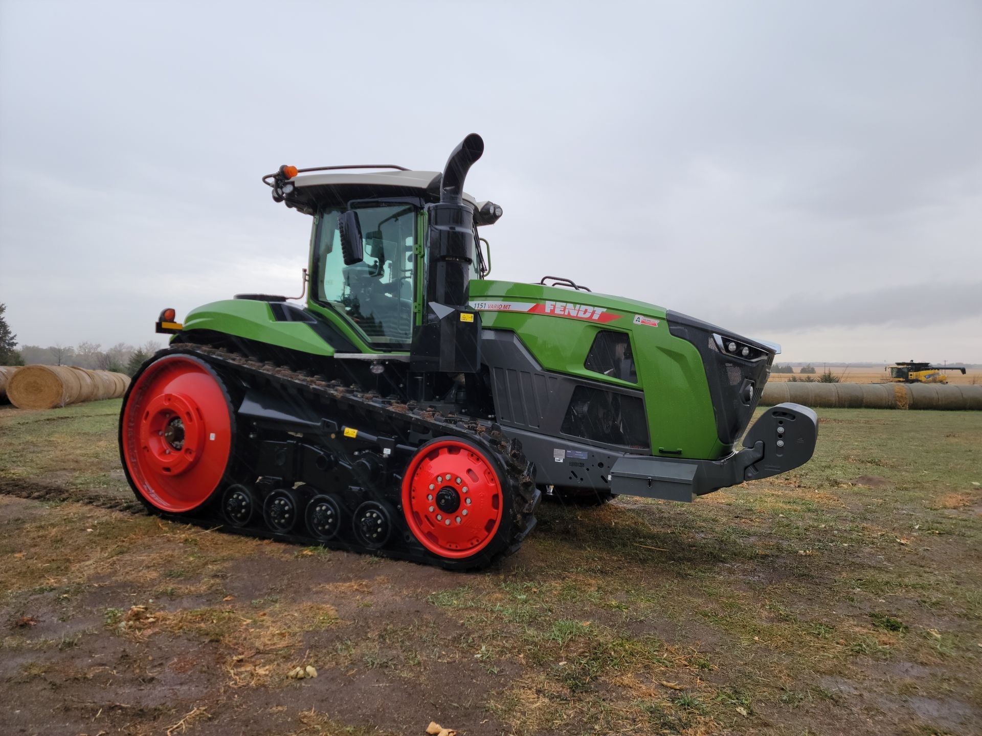 Green and black Fendt tractor with red wheels on a muddy field under a cloudy sky.