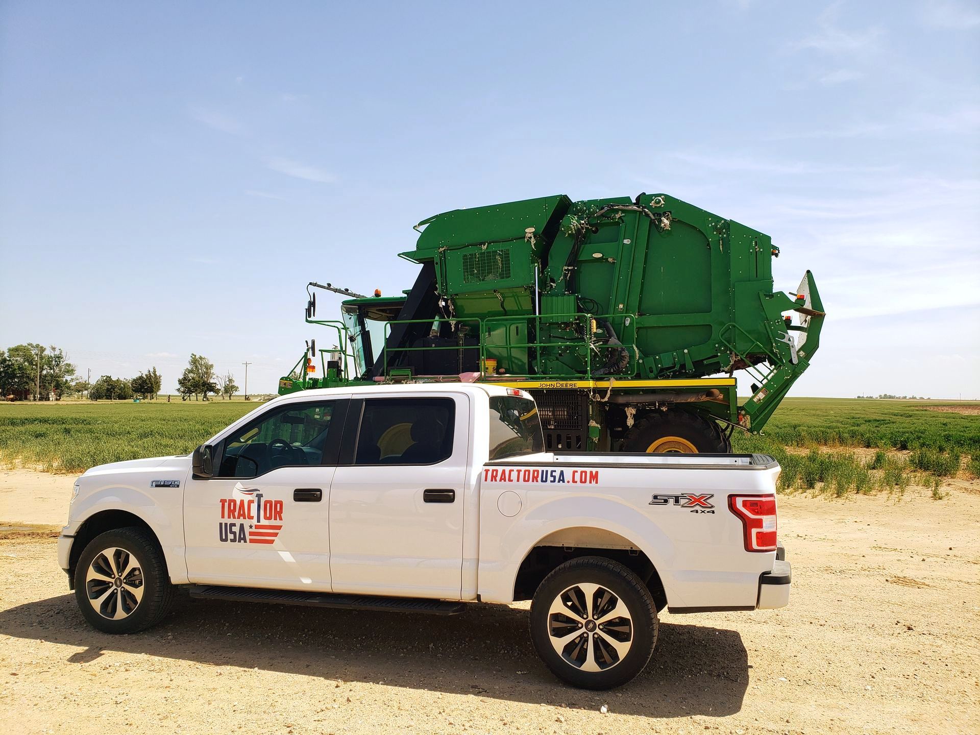 White pickup truck transporting green farm machinery on a sunny day.