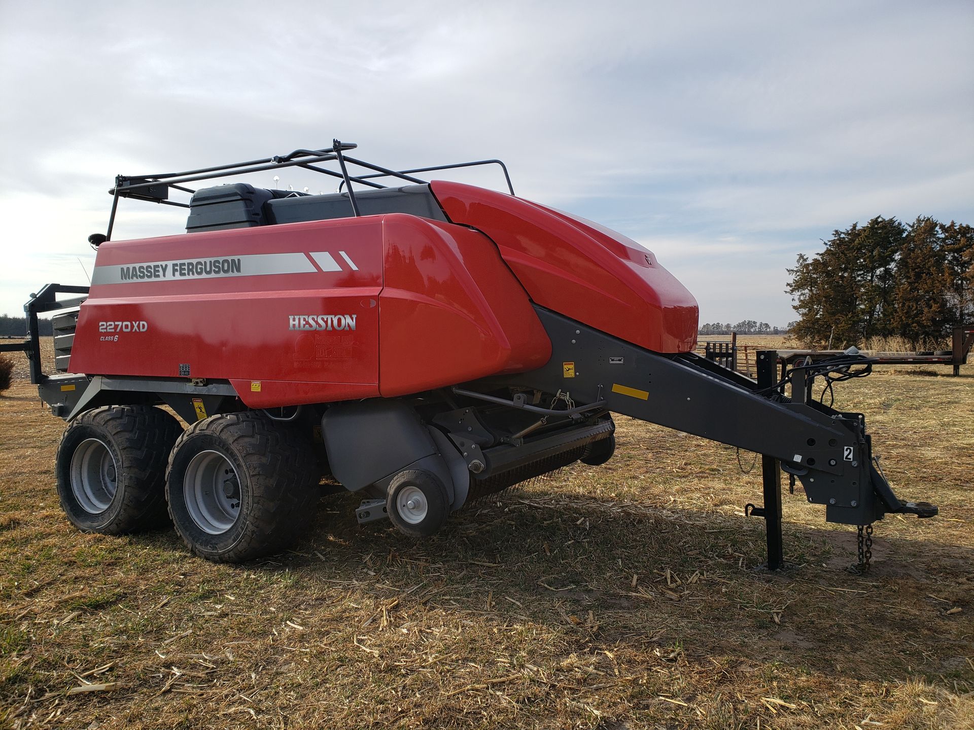 Red Massey Ferguson round baler on a field, preparing hay.