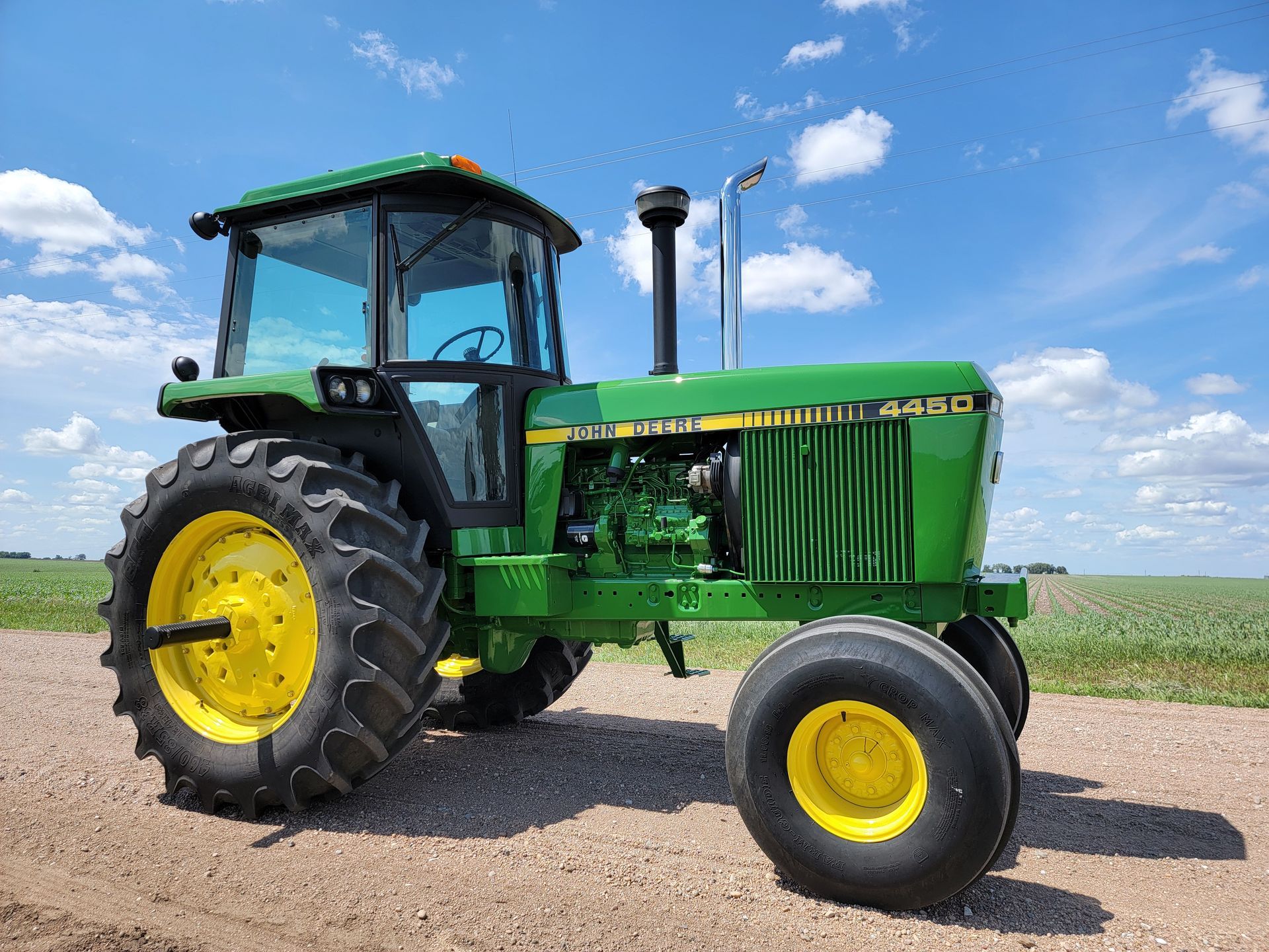 Green and yellow John Deere 4450 tractor in a field under a blue sky.