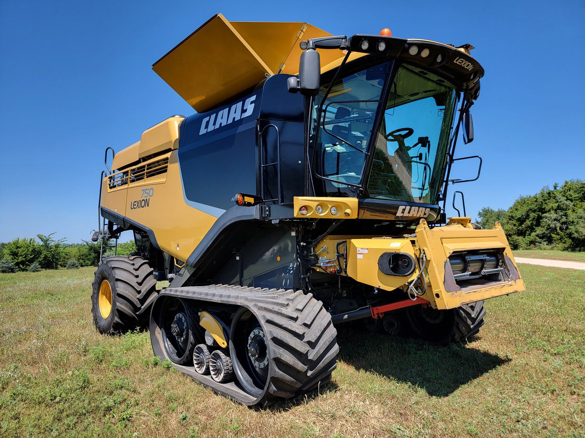 Yellow and black Claas combine harvester with tracks in a field.