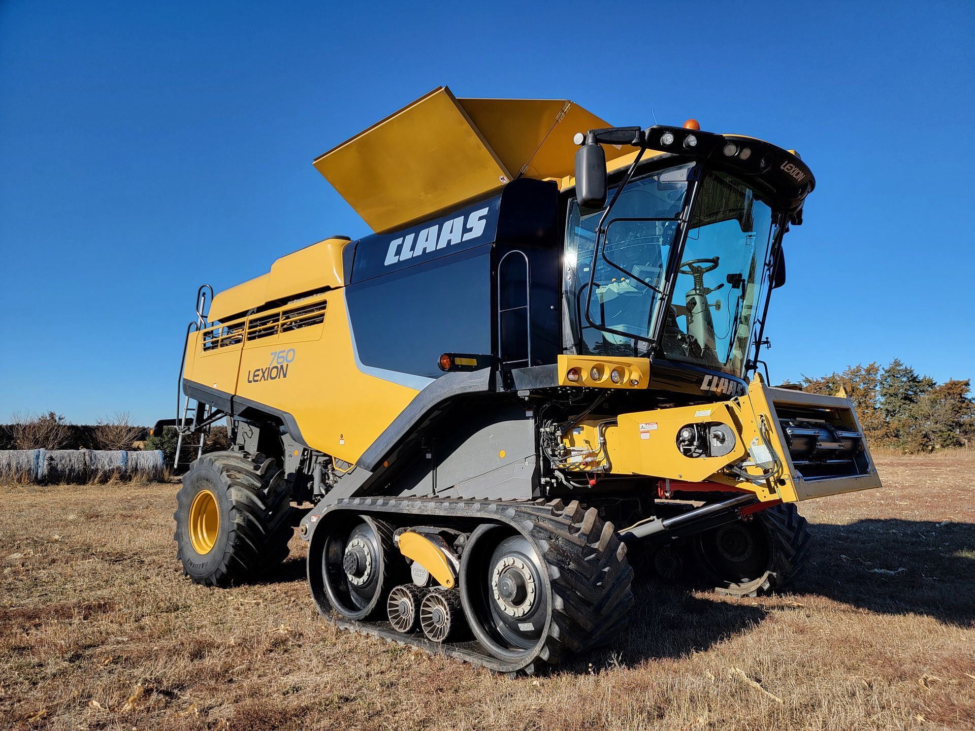 Yellow and black CLAAS combine harvester with tracks in a field.