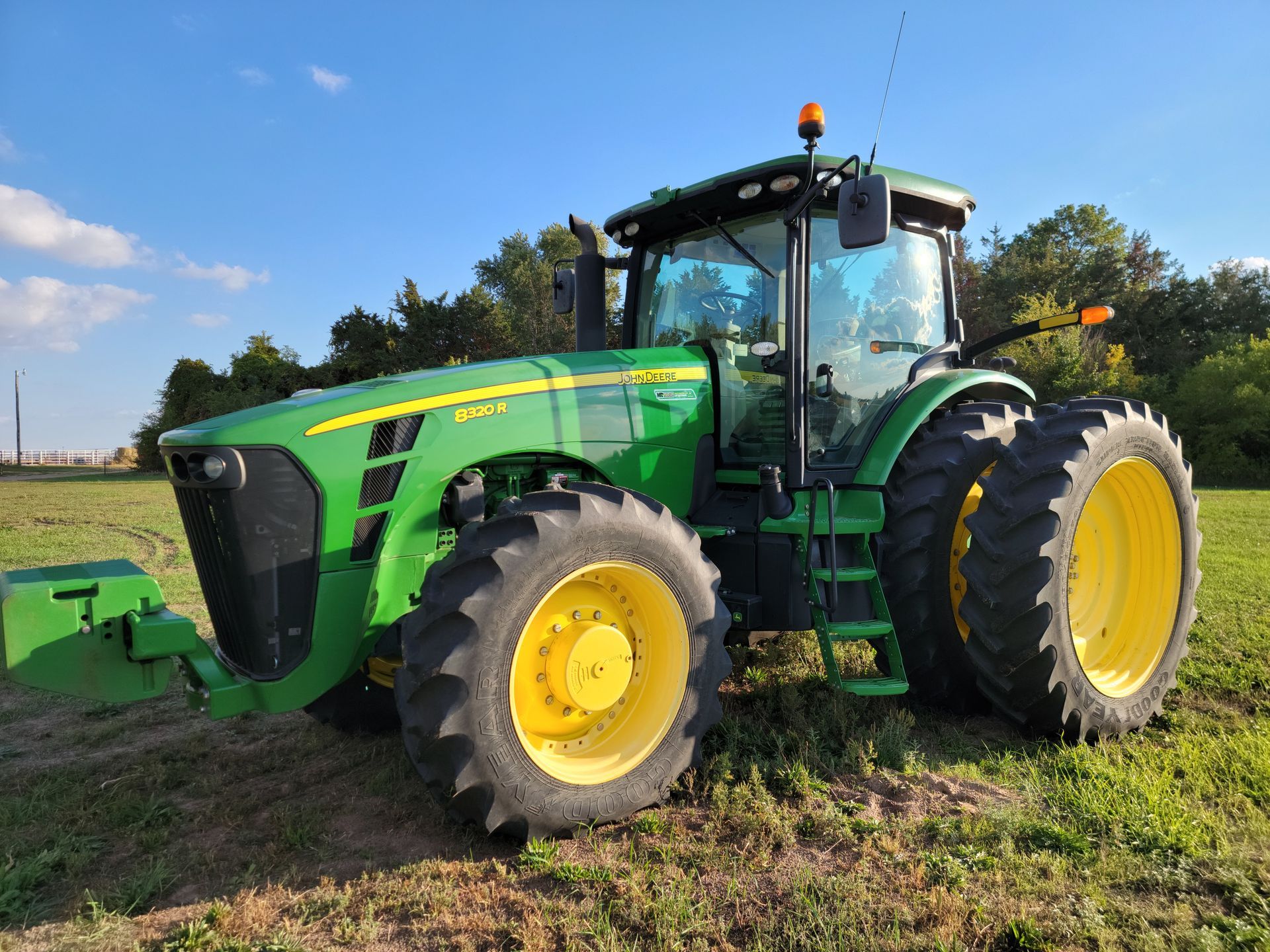 Green John Deere tractor in a grassy field under a blue sky.