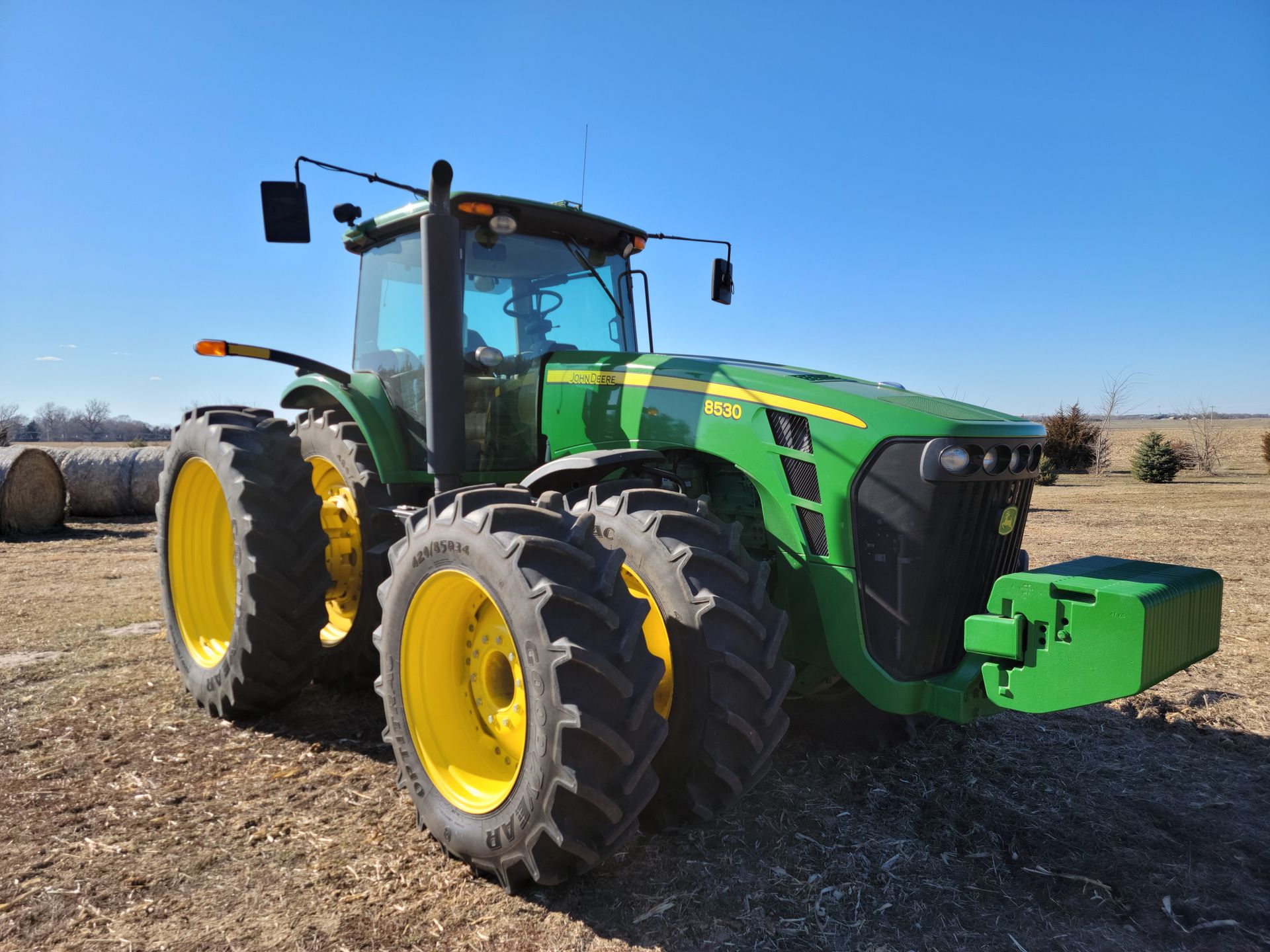 Green and yellow John Deere tractor on a farm field under a blue sky.