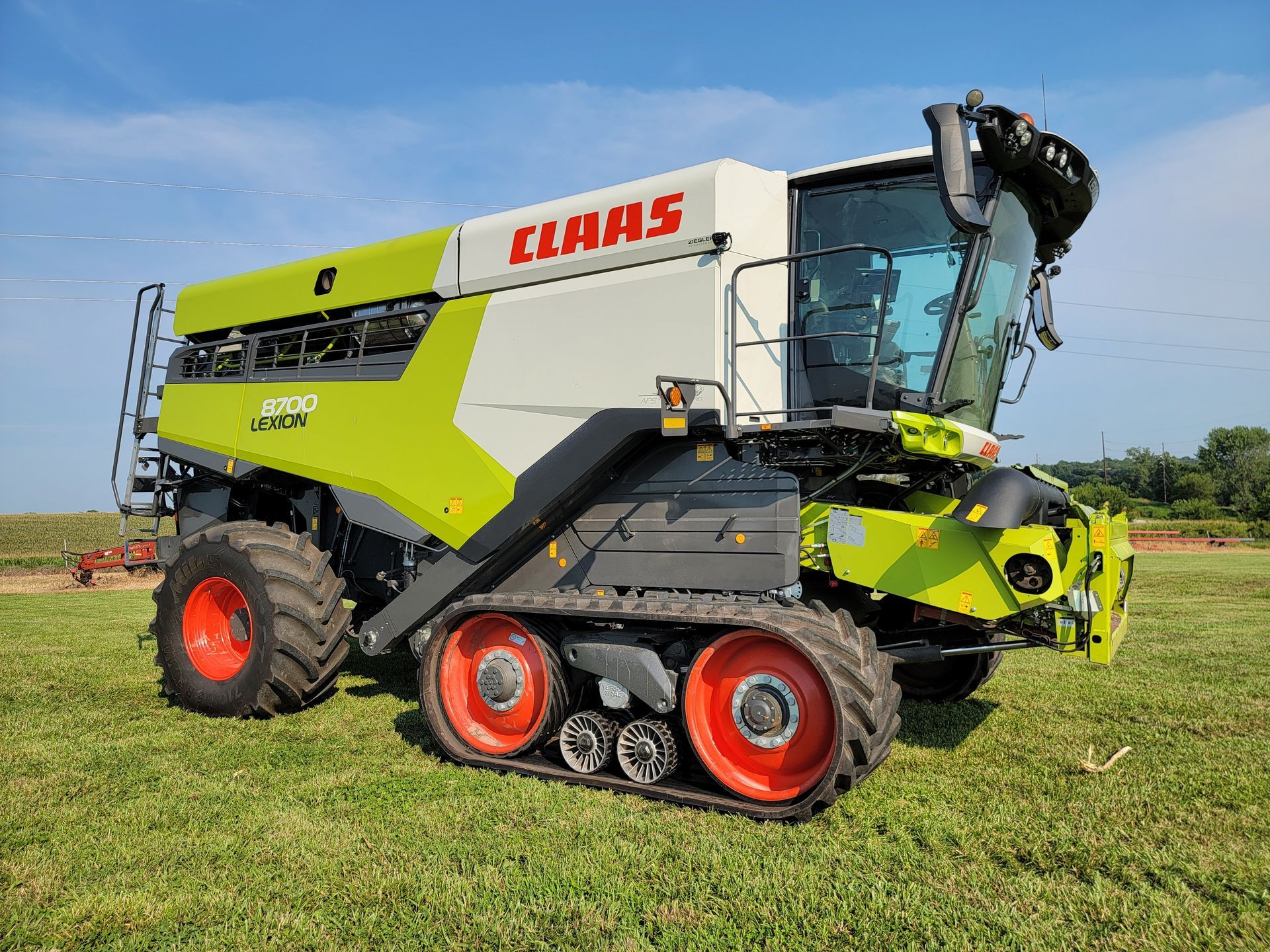 CLAAS combine harvester on a grassy field with tracks, white, green, and red colors, under a blue sky.