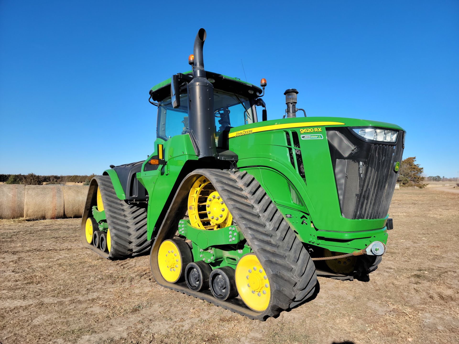 Green John Deere tractor with tracks in a field on a sunny day.