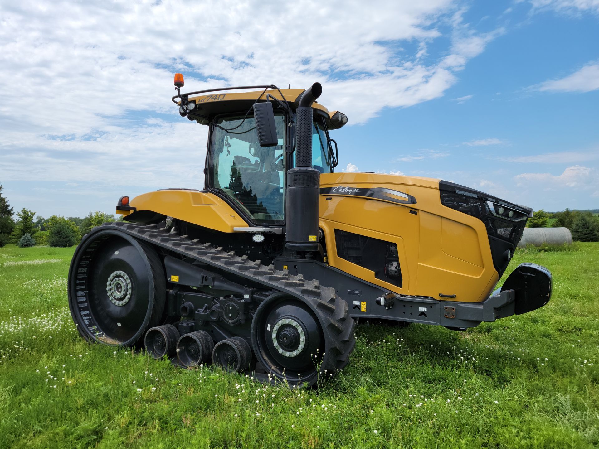 Yellow Challenger tractor with tracks in a grassy field under a blue sky.