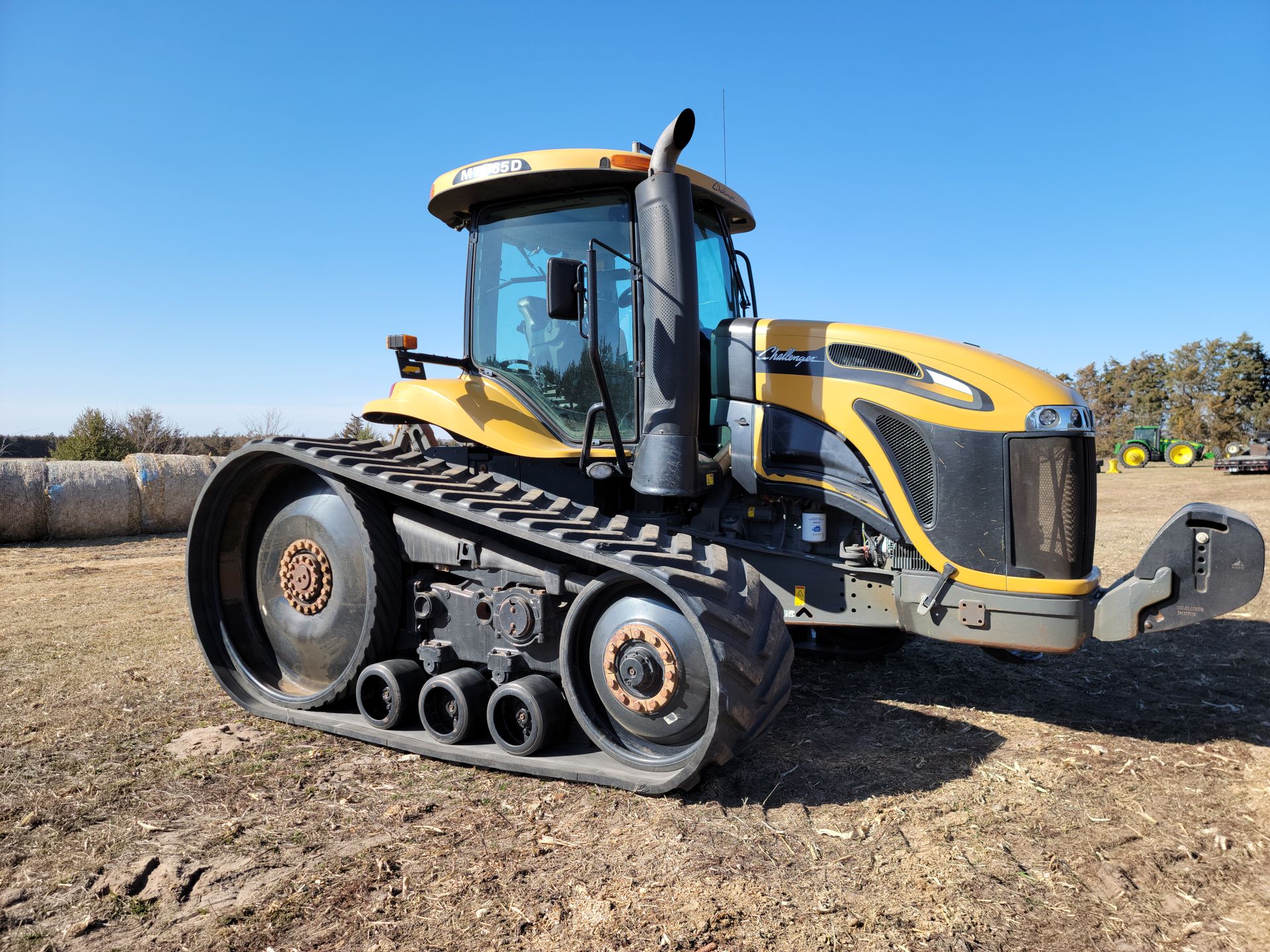 Yellow Challenger track tractor on a farm field with a blue sky in the background.