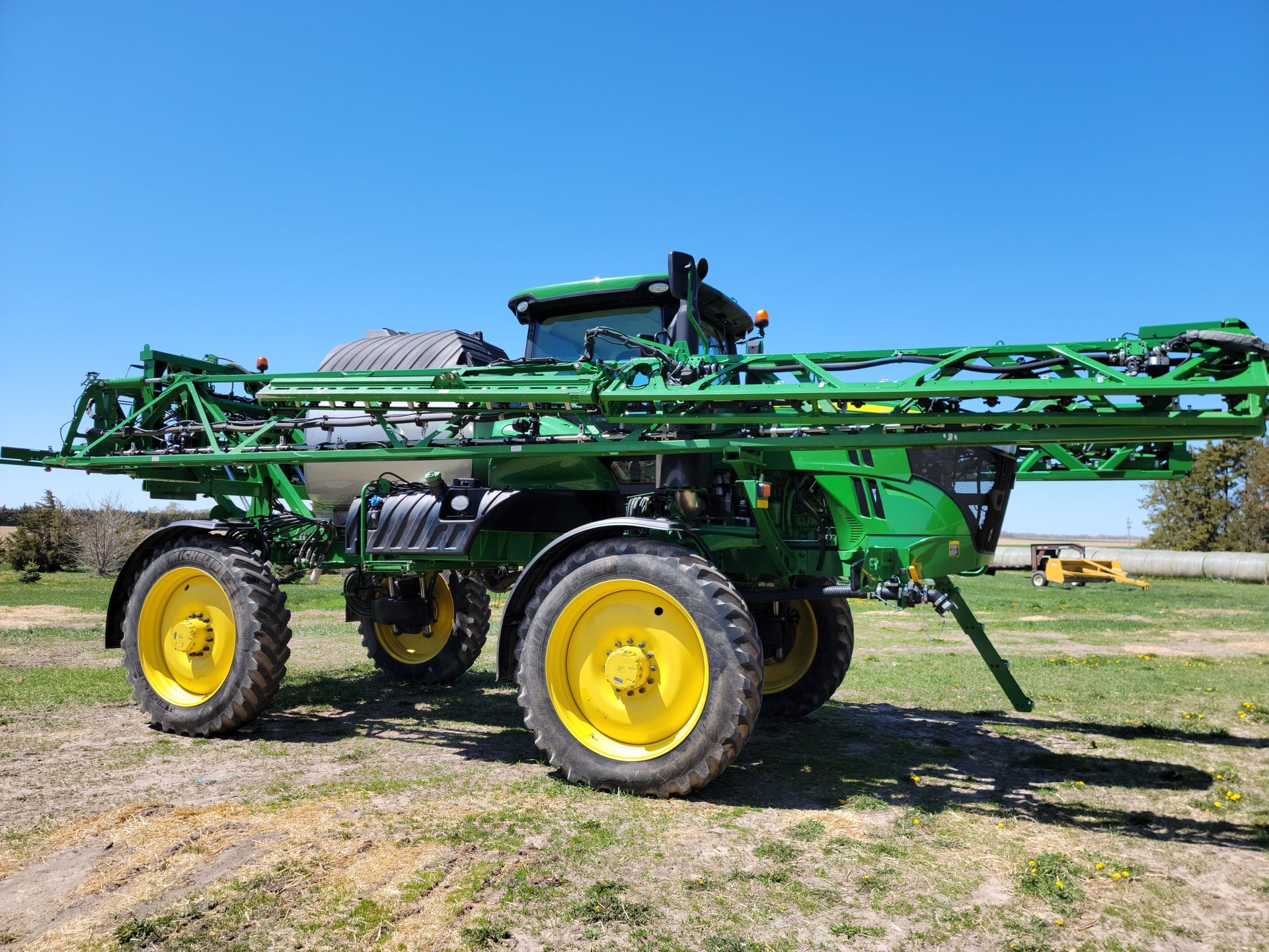 Green and yellow John Deere agricultural sprayer in a field.