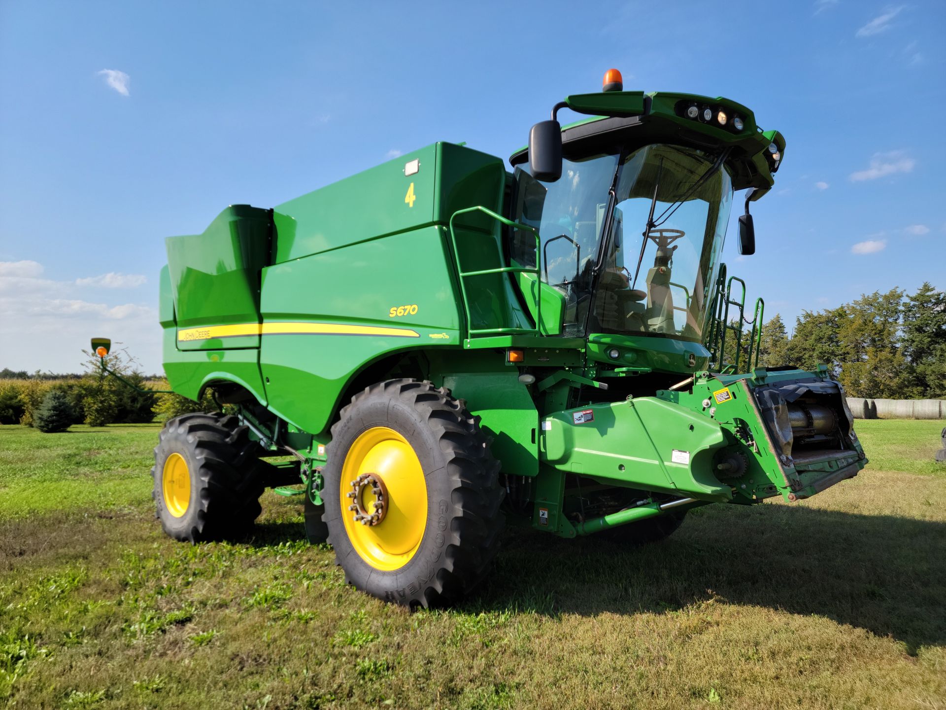 Green and yellow John Deere combine harvester in a field under a blue sky.