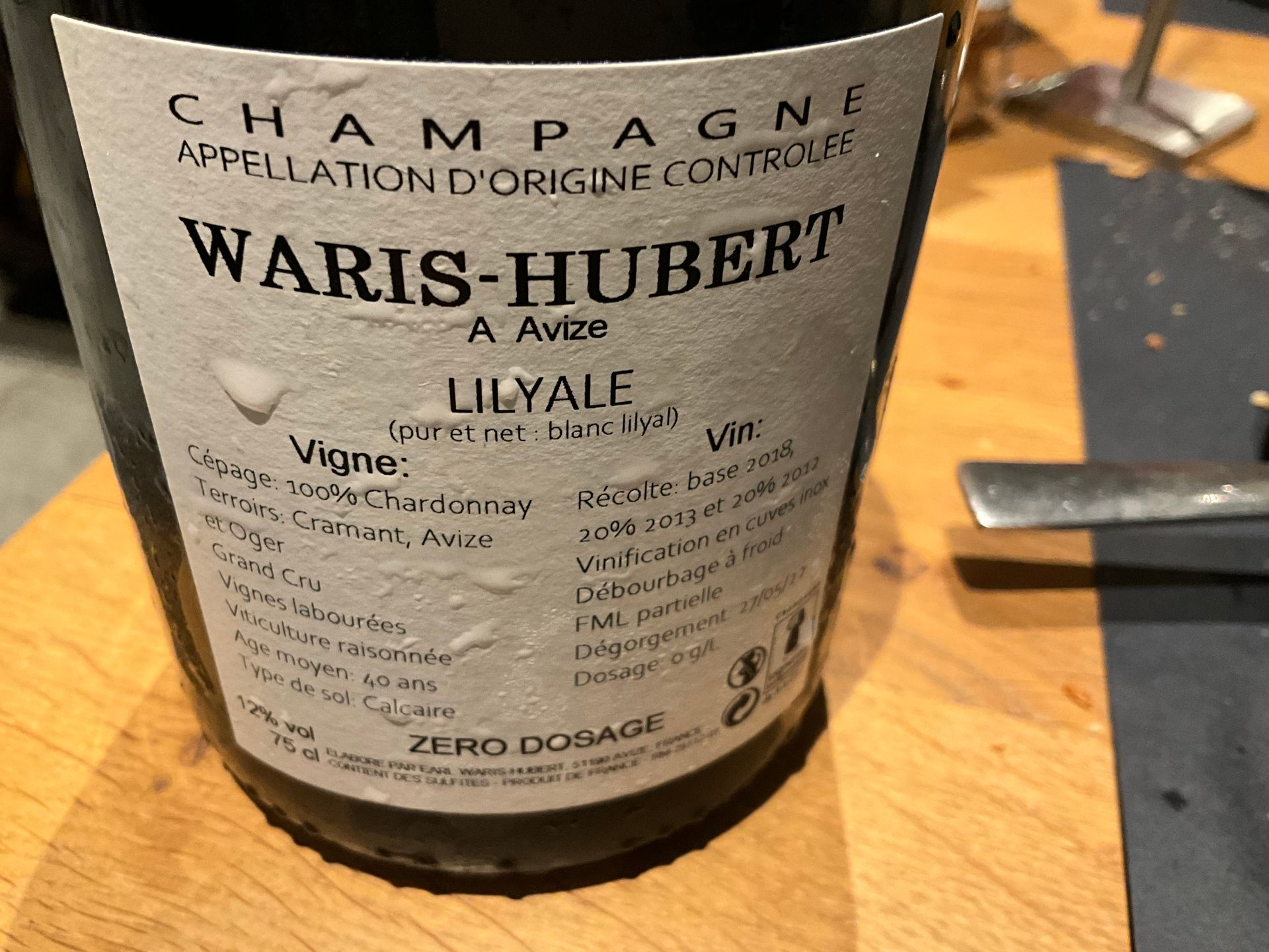 eine Flasche Waris-Bubert Champagner  Champagne Waris-Hubert Cuvée Lilyale Blanc de Blancs 
steht auf einem Holztisch