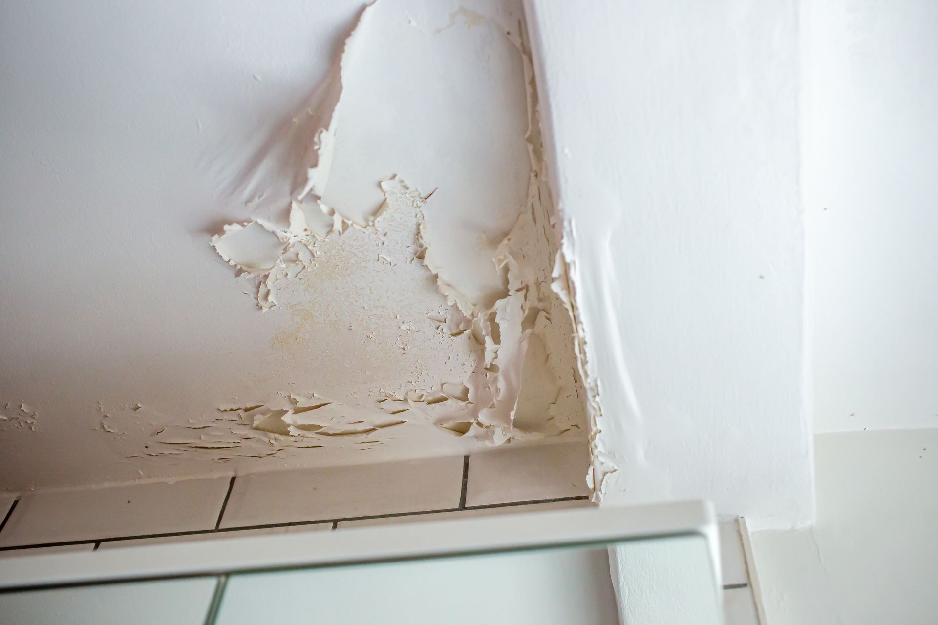 White ceiling with peeling paint above a tiled surface, indicating water damage.