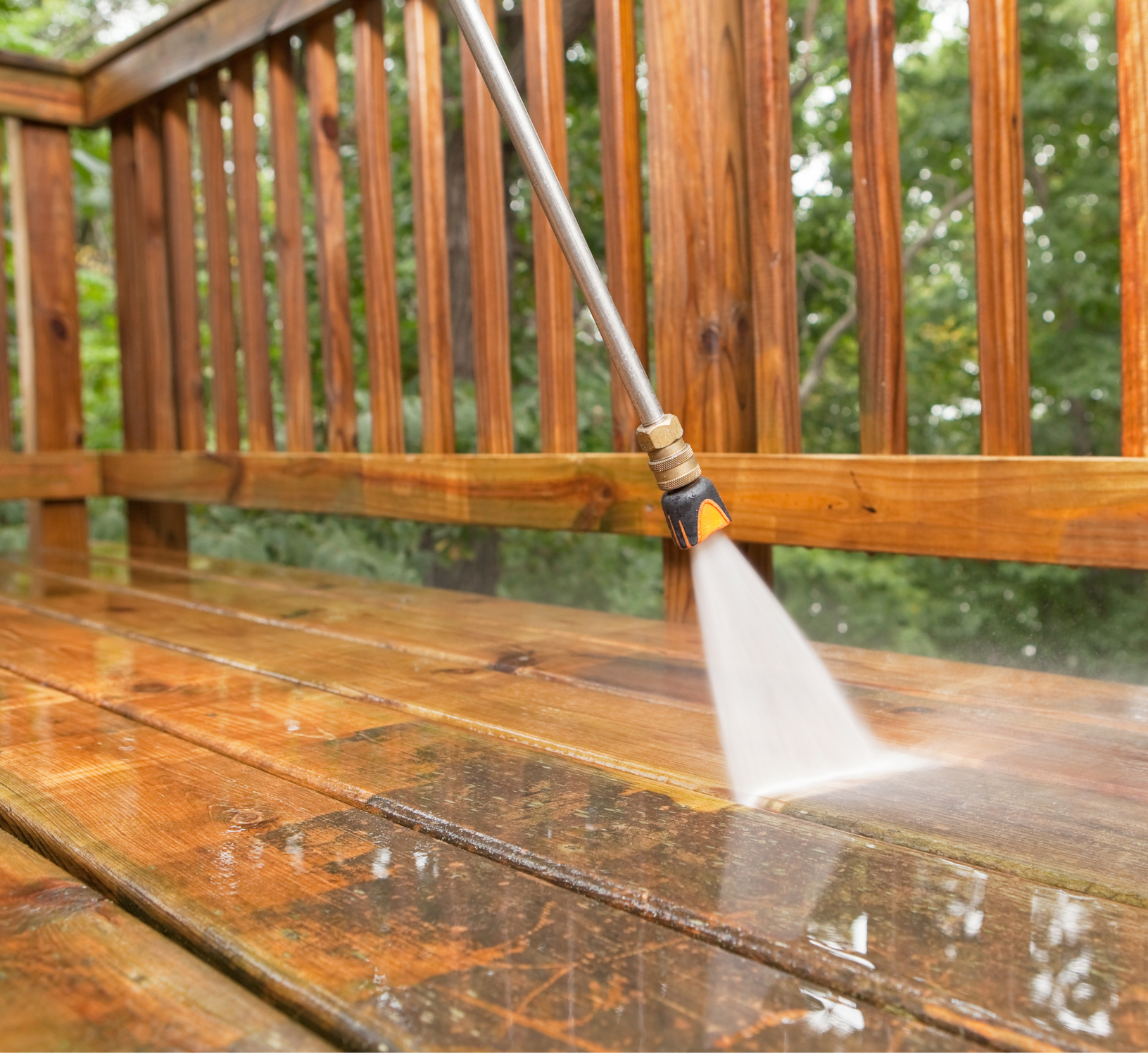 A person is using a high pressure washer to clean a wooden deck.