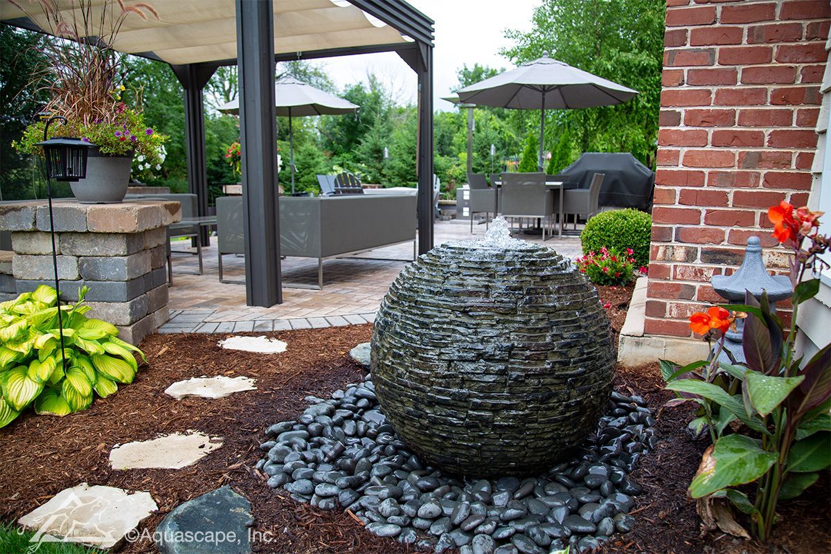 Outdoor patio with a bubbling stone fountain surrounded by landscaping and seating areas.