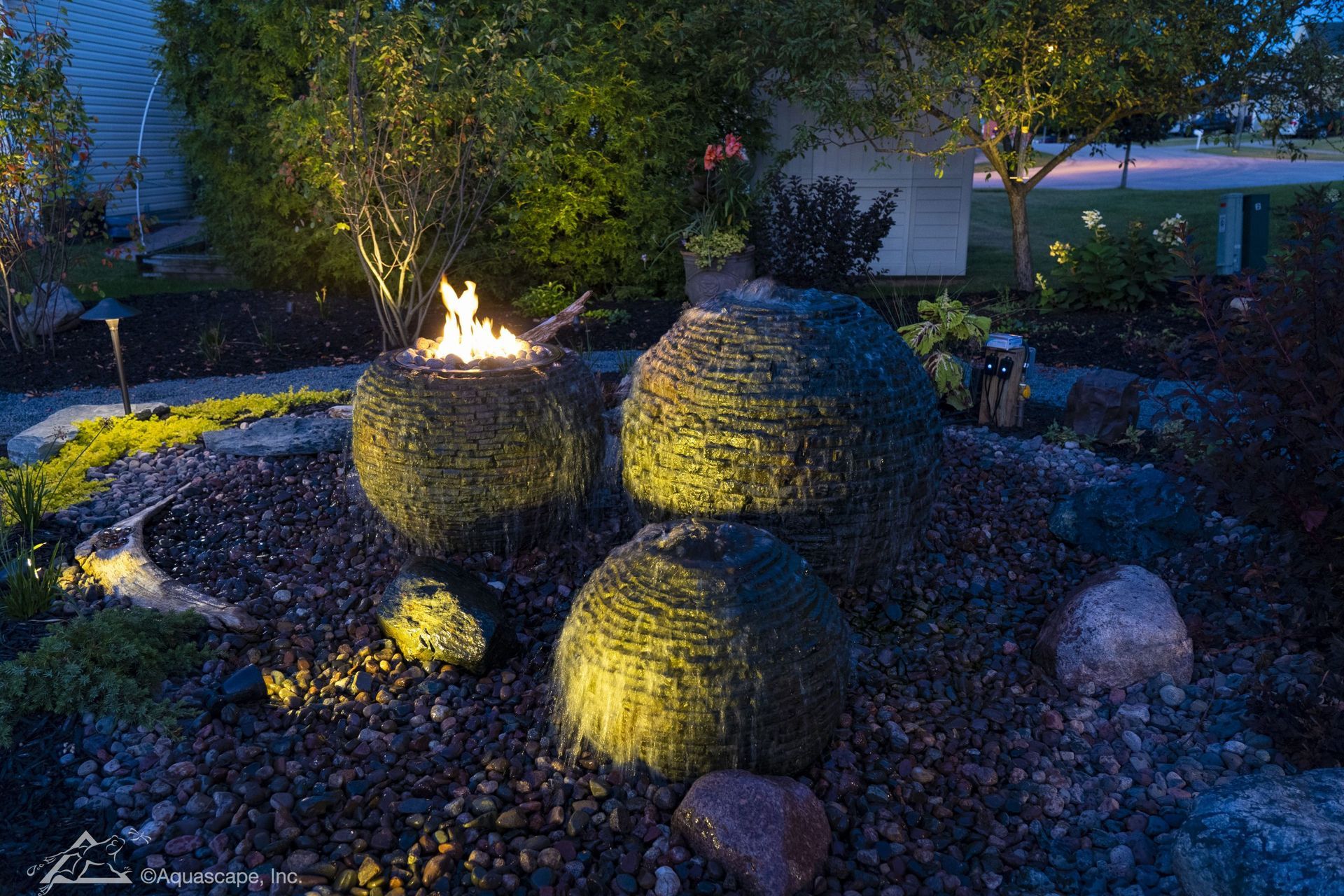 Three spherical, moss-covered structures in a garden bed with a fire pit, illuminated at night.