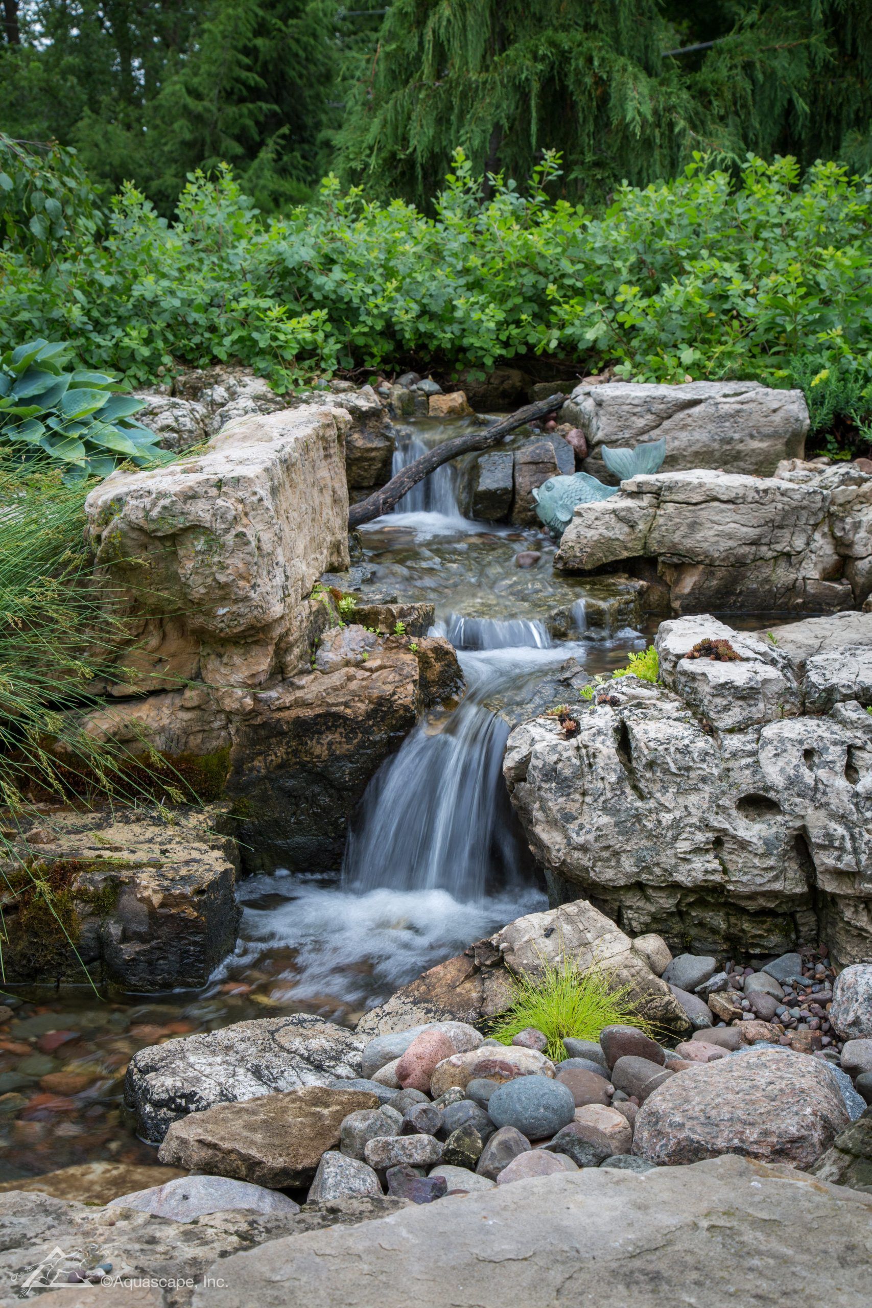 A small waterfall cascades over rocks, surrounded by greenery.