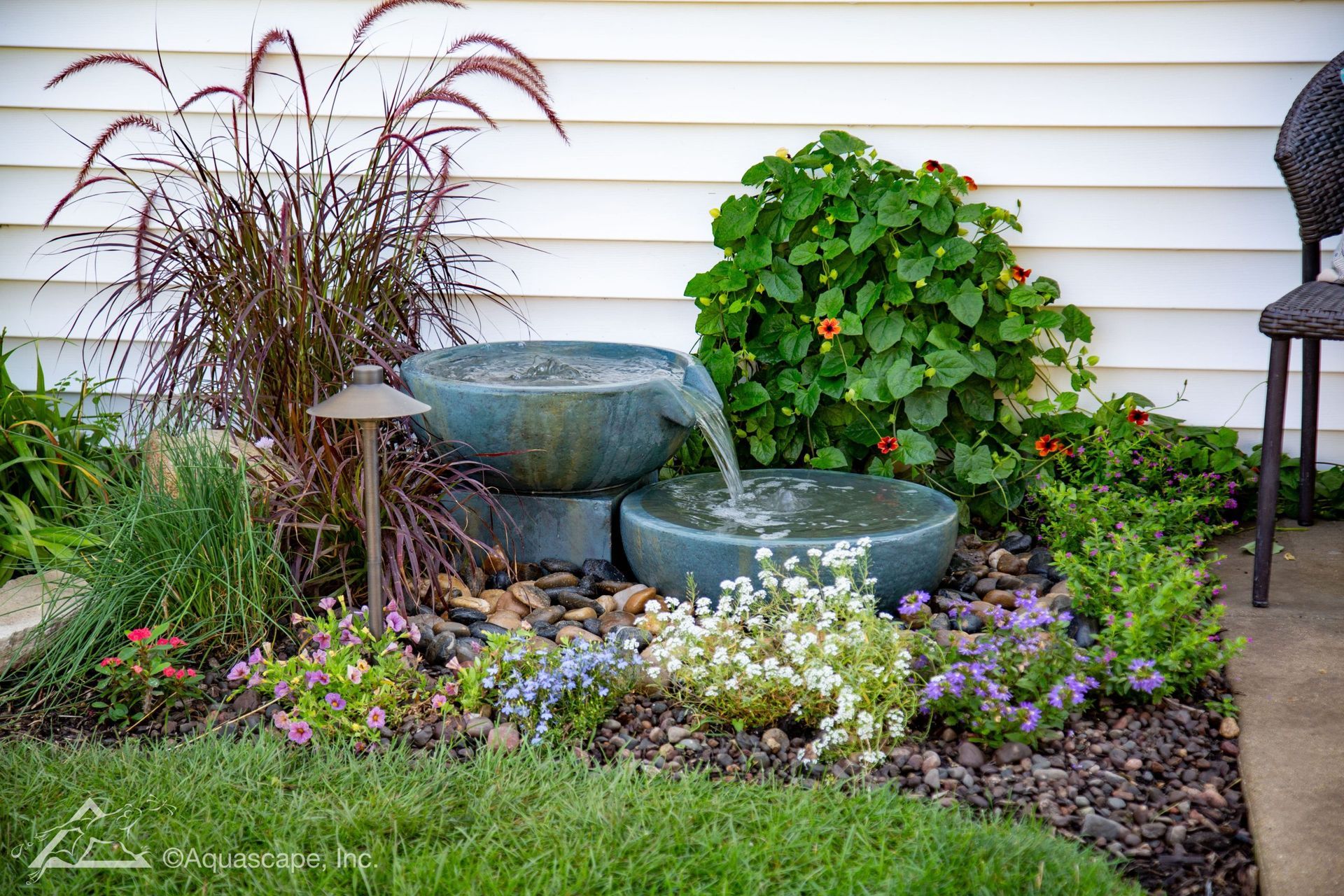 Water fountain with cascading bowls surrounded by plants and landscaping rocks.