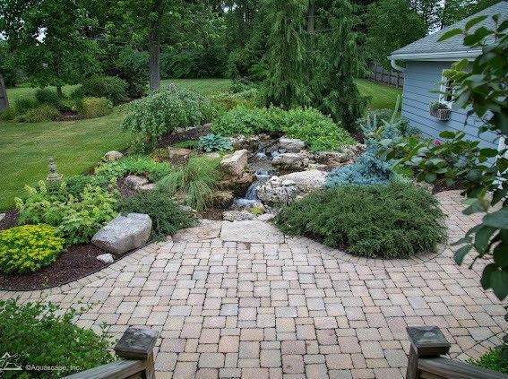 Brick patio leads to a garden with a waterfall and lush greenery.