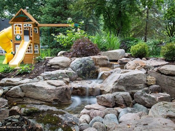 Backyard with a small waterfall feature and a wooden playset with a slide.