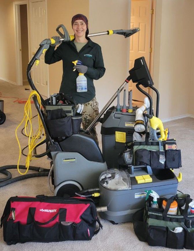 Person in uniform holding carpet cleaning equipment, standing in room with carpet.